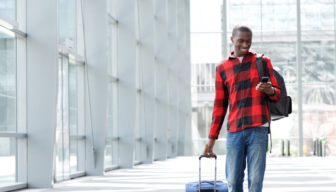 Traveller booking a TransBaggage luggage collection on a smartphone while walking with a suitcase